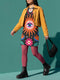 A short-sleeve, above-the-knee t-shirt dress with a straight, structured fit. The dress has a true black background featuring a bold, vibrant graphic pattern. The center displays a large blue and white evil eye surrounded by a bright orange wavy sunburst with a white jagged border. Above and below the eye are bright pink daisy flowers with orange centers, scattered white four-petal stars, and wavy blue and teal green leaf shapes. The fabric is thick, smooth, and holds its clean shape.