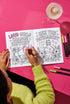 A 8.5 by 11 inch softcover coloring book titled The Feminist Rage Coloring Book For Cute Loud Unhinged Women. The black cover features vibrant pink and green typography, a fanged heart engulfed in flames, pink roses, and crescent moons. The back cover displays a heart pierced by a dagger and text reading Your feelings are valid your rage is too. Inside pages contain black and white line art with bold feminist quotes, floral borders, potions, coffins, and edgy witchy illustrations.