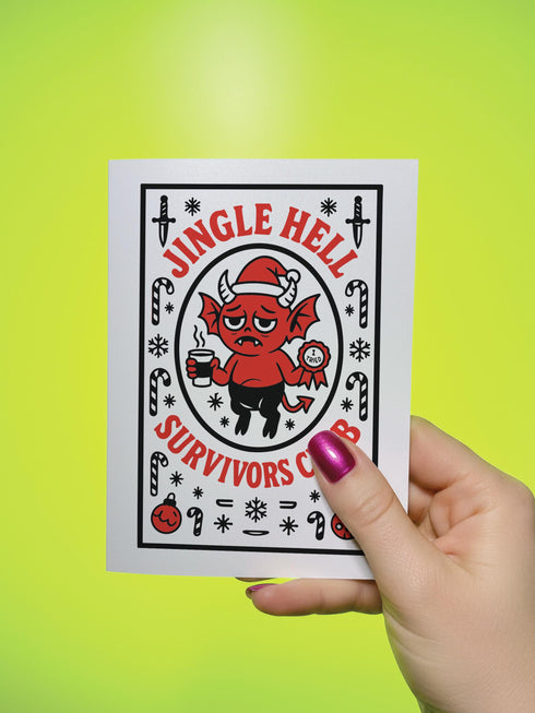 A 5x7 pearlescent shimmer folded greeting card featuring the Jingle Hell Survivors Club design. The front is a illustration of a grumpy red devil imp character, wearing a small Santa hat, holding a coffee cup, and a circular 'I Tried' merit badge. The overall aesthetic is maximalist dark humor and spooky cute. This anti-Christmas card is perfect for those needing relief from holiday stress. Inside text references surviving tolerable relatives, strong eggnog, and merciful hangovers.
