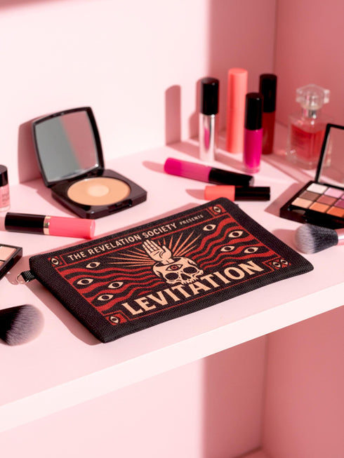 A rectangular makeup bag featuring a vibrant psychedelic print with gothic elements. The fabric texture is clearly visible showing a woven linen-like polyester grain. A black zipper runs across the top edge with a black detachable nylon wrist strap clip on the side, showcasing the approximately nine by six inch dimensions. The print includes high contrast neon colors and trippy swirling patterns typical of maximalist decor.