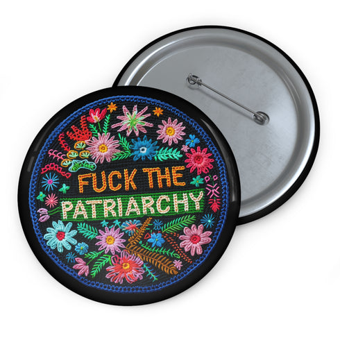 Circular black pinback button with "FUCK THE PATRIARCHY" in orange and mint green text, surrounded by embroidery-style flowers in pink, blue, and red with green foliage and blue border. Folk art feminist protest pin with glossy finish and safety pin backing in 2" and 3" sizes.