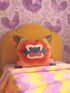 a vibrant and colorful bedroom scene, with a yellow headboard and a pillow adorned with a bold, graphic design. The pillow has a mouth and teeth motif, adding a playful and whimsical touch to the room's decor. The bed is covered in a colorful striped blanket, complementing the overall lively atmosphere of the space.