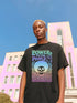 A detailed view of a black unisex graphic t-shirt made of soft cotton, shown flat. The shirt features a large, rectangular design on the chest inspired by 70s psychedelic protest art. The words "POWER TO THE PEOPLE" are printed at the top in a thick, rounded, groovy font. Below the text is a stylized human skull with a large, perfectly round afro hairstyle. The entire design, including the text, skull, and afro, is filled with a vibrant color gradient that shifts from deep purple to hot pink.