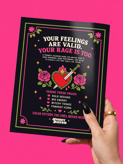 A 8.5 by 11 inch softcover coloring book titled The Feminist Rage Coloring Book For Cute Loud Unhinged Women. The black cover features vibrant pink and green typography, a fanged heart engulfed in flames, pink roses, and crescent moons. The back cover displays a heart pierced by a dagger and text reading Your feelings are valid your rage is too. Inside pages contain black and white line art with bold feminist quotes, floral borders, potions, coffins, and edgy witchy illustrations.