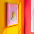 A fine art print of a glamorous rubber duck styled like Marilyn Monroe, with short curled blonde hair and soap bubbles. Displayed in a gold ornate frame against a pink wall with orange bead curtains.