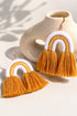 a pair of earrings with orange and white tassels, placed on a white surface next to a white vase.