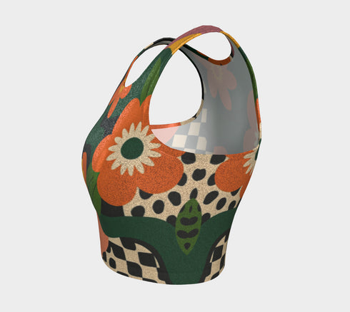 Cropped racerback tank top featuring bold retro floral print with orange and yellow mod flowers, green leaves, black and white checkerboard pattern, and abstract wavy designs. Fitted athletic style crop top in vibrant 70s inspired botanical print with performance fabric construction. Women's festival rave wear cropped camisole with psychedelic flower power design perfect for summer concerts, Y2K fashion looks, and alternative streetwear styling.