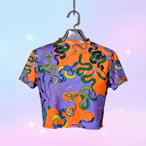 A vibrant see-through mesh crop top with a high mock neck and short sleeves. The shirt features a bold, all-over snake print pattern with colorful green, blue, yellow, and black serpents on a striking orange and purple color-block background. This Y2K-style top is a statement piece of witchy, goth, and alternative clothing, perfect for a maximalist rave outfit or edgy festival fashion from a black owned shop.