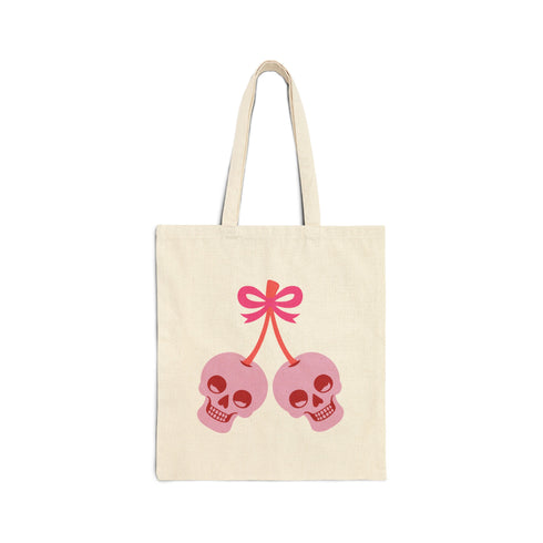 Canvas tote bag featuring pink skull cherries design. Two pink skulls connected by red stem and bow. Quirky gothic-inspired graphic on cream background. Stylish, edgy accessory for everyday use. Perfect for alternative fashion lovers.