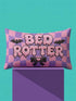 Pastel goth lumbar pillow, 20 by 12 inches, with a pink and lavender purple wavy checkerboard background. The words Bed Rotter appear in dripping pink bubble letters with a faux embroidery thread texture and black outlines. Two black bats with pink stitch details flank the text, and a black bow with a pink heart center sits below. Double sided flat print that mimics raised embroidery on linen feel polyester with a hidden zipper, insert included.