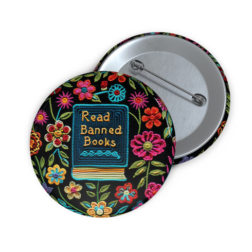 Round pinback button featuring a teal book with "Read Banned Books" in gold lettering on black background, surrounded by vibrant embroidery-style flowers in pink, orange, and blue. Literary protest pin with glossy finish and safety pin backing, available in 2" and 3" sizes for bookish fashion statements.