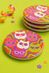 A close-up photograph of a glossy round ceramic coaster featuring a retro 70s psychedelic design. The artwork displays a cluster of six stylized cat face illustrations, each wearing a different pair of sunglasses including retro round and cat-eye shapes. The cats are colored in solid shades of white, hot pink, purple, and lime green. They are set against a vibrant background of wavy, swirling lines in bright orange, red, and purple. The top surface has a highly reflective clear glaze.