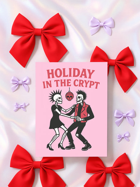 A 5x7 inch greeting card with a vibrant pink background and red retro text reading 'HOLIDAY IN THE CRYPT'. The illustration shows a male and female punk rock skeleton dancing under a red skull disco ball. The female skeleton has a mohawk and wears a black dress. The male skeleton has a mohawk and wears a black jacket with a red vest. Inside, the message reads, 'From our crypt to yours. Eat, drink, and be scary.' The style is a graphic, punk aesthetic.