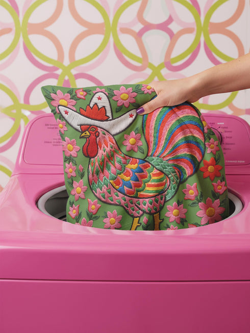 Square throw pillow cover with a printed faux embroidery design of a rooster wearing a white cowboy hat with red stars on a grass green background. The western chicken has a red comb and wattle, yellow beak and feet, and layered feathers in pink, green, orange, blue, and yellow with a rainbow striped tail. Pink and red flowers with yellow centers frame the bird. The stitched look is a flat 2D print on a smooth linen feel polyester cover with a hidden zipper, not raised embroidery.
