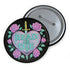 Glossy black pinback button featuring embroidered-style artwork of a pastel purple heart that reads “Read or Die” pierced by a sword and surrounded by roses; shown on books, graffiti, and lace backgrounds.