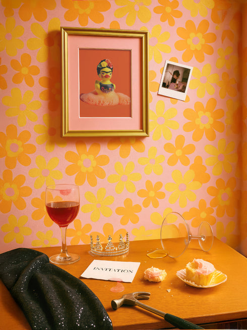 A vibrant fine art print of a rubber duck inspired by Frida Kahlo, complete with bold unibrow, floral crown, and traditional embroidered blouse. Framed in a red sculptural frame, the duck floats in orange-tinted bubbles against a deep orange backdrop and violet wall.