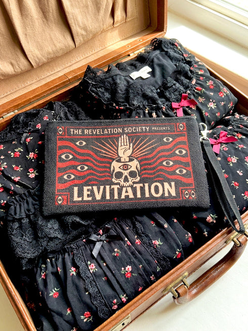 A rectangular makeup bag featuring a vibrant psychedelic print with gothic elements. The fabric texture is clearly visible showing a woven linen-like polyester grain. A black zipper runs across the top edge with a black detachable nylon wrist strap clip on the side, showcasing the approximately nine by six inch dimensions. The print includes high contrast neon colors and trippy swirling patterns typical of maximalist decor.