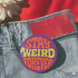A round metal pin button with a glossy finish and a vibrant purple background. The phrase 'STAY WEIRD FOREVER' is written across the center in a wavy, psychedelic 70s-style font. The words 'STAY' and 'FOREVER' are a bold, bright orange, while the word 'WEIRD' is rendered in a contrasting, electric chartreuse lime green. The button has a smooth, scratch-resistant mylar surface covering the design. The pin is shown in its 2-inch and 3-inch variations, highlighting its circular shape and durable construction.