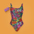 A colorful one-piece swimsuit features a vibrant, quirky pattern with cherries, cartoon eyes, and playful designs on a dark background.
