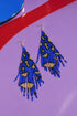 A pair of blue and gold beaded earrings with a leopard print pattern, displayed on a purple background with a red and blue striped pattern.