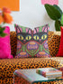 A square decorative pillow cover featuring a vibrant, symmetrical flat printed design that mimics the look of textured embroidery. Two black cats with large yellow eyes and pink noses face forward against a bright red background. Below the cats are large purple and pink flowers with green stems. Above the cats are green cactus shapes. The artwork uses bold, colorful outlines to create an optical illusion of stitching, though the fabric itself is smooth.