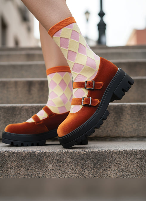A pair of feet wearing orange and pink checkered socks and black platform shoes, walking up a set of stairs.