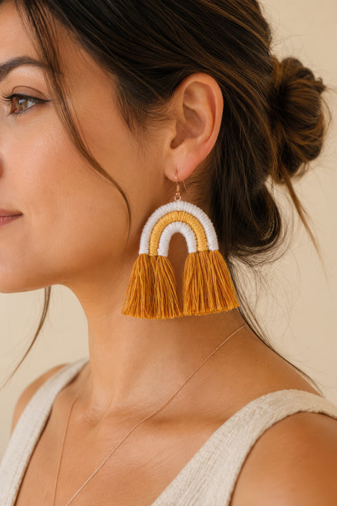 A woman with brown hair wearing a white top and a pair of yellow and white tassel earrings.