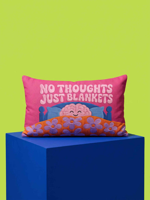A bright magenta pink rectangular lumbar pillow cover featuring a flat 2D printed faux embroidery design. The printed illusion shows light pink bubble text reading NO THOUGHTS JUST BLANKETS. Below the text is a cartoon pink brain with a happy face, tucked into a blue bed with blue pillows. The brain is covered by a textured-looking orange blanket decorated with light purple daisies. The entire design is a smooth printed trompe l'oeil stitch effect, not real woven or stitched texture.