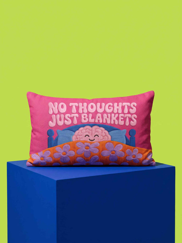 A bright magenta pink rectangular lumbar pillow cover featuring a flat 2D printed faux embroidery design. The printed illusion shows light pink bubble text reading NO THOUGHTS JUST BLANKETS. Below the text is a cartoon pink brain with a happy face, tucked into a blue bed with blue pillows. The brain is covered by a textured-looking orange blanket decorated with light purple daisies. The entire design is a smooth printed trompe l'oeil stitch effect, not real woven or stitched texture.