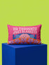 A bright magenta pink rectangular lumbar pillow cover featuring a flat 2D printed faux embroidery design. The printed illusion shows light pink bubble text reading NO THOUGHTS JUST BLANKETS. Below the text is a cartoon pink brain with a happy face, tucked into a blue bed with blue pillows. The brain is covered by a textured-looking orange blanket decorated with light purple daisies. The entire design is a smooth printed trompe l'oeil stitch effect, not real woven or stitched texture.