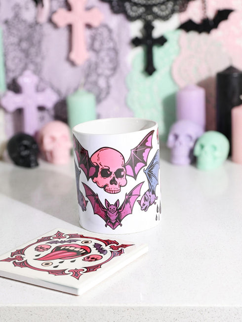 White porcelain 11oz mug and matching 4x4 inch square ceramic coaster set featuring a vibrant, maximalist full-wrap pattern. The design illustrates glossy pink vampire lips with white fangs and red tongues, interspersed with floating eyeballs, purple bats, and small pink skulls against a white background. The mug features a glossy finish and C-handle. The coaster has a matching glazed ceramic top and a brown cork backing. High-contrast pop-art style with pink, purple, and black details.