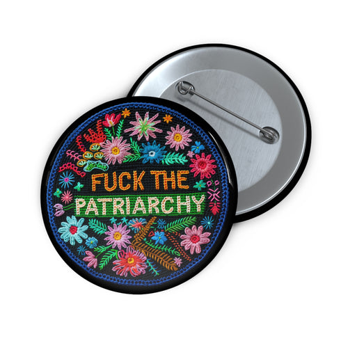 Circular black pinback button with "FUCK THE PATRIARCHY" in orange and mint green text, surrounded by embroidery-style flowers in pink, blue, and red with green foliage and blue border. Folk art feminist protest pin with glossy finish and safety pin backing in 2" and 3" sizes.
