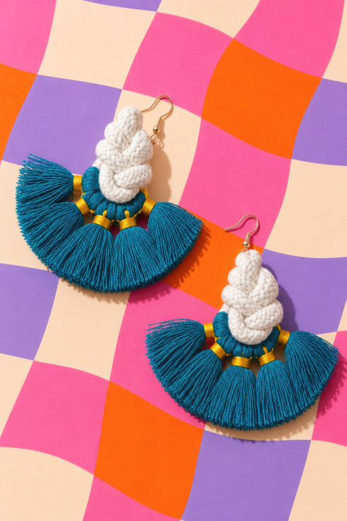 a pair of earrings with blue and white tassels, set against a colorful checkered background.