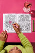 A 8.5 by 11 inch softcover coloring book titled The Feminist Rage Coloring Book For Cute Loud Unhinged Women. The black cover features vibrant pink and green typography, a fanged heart engulfed in flames, pink roses, and crescent moons. The back cover displays a heart pierced by a dagger and text reading Your feelings are valid your rage is too. Inside pages contain black and white line art with bold feminist quotes, floral borders, potions, coffins, and edgy witchy illustrations.