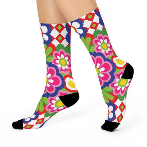 Mid-calf crew sock with a bold 70s psychedelic floral print. The design mixes a red and white diagonal checkerboard with oversized retro flowers, including white daisies with bright yellow centers and a large hot pink bloom with a white inner layer, set over a royal blue background with green leafy foliage. The toe and heel are solid black. The fabric is a soft, stretchy printed knit, made as a one-size unisex statement sock for maximalist and dopamine dressing looks.