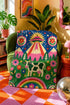 A rectangular velveteen minky blanket with a bright, maximalist design. The top half features a vibrant blue sky with a pink, green, and yellow UFO beaming rays down over hot pink snow-capped mountains. The bottom half shows a grassy green field with a white cow covered in dark spots, surrounded by large, colorful red, pink, and blue retro flowers, pine trees, and a rainbow arch at the very bottom. The reverse side is a fluffy off-white sherpa.