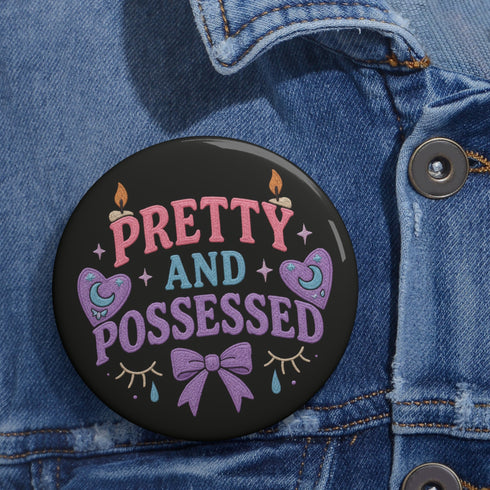 Glossy black pinback button featuring pastel-style text that reads “Pretty and Possessed” with a bow, candles, hearts, and sparkles.