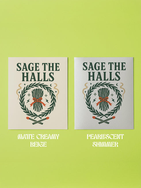 A detailed folk-art style illustration of a "Sage the Halls" holiday greeting card. The design features a bundle of sage smudge sticks tied with a red ribbon at the center of a dark green wreath. The wreath is accented with small crescent moons, stars, and smoke swirls. Below the wreath are two crossed matches with red tips. The card is printed on creamy beige paper with bold, dark green serif text. This funny spiritual and witchy Yule card is a unique pagan greeting for energy cleansing.