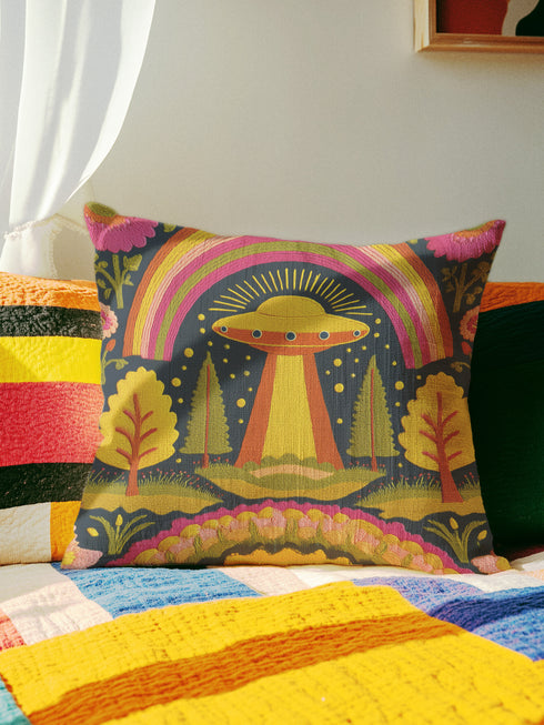 a colorful throw pillow with a vibrant, alien-like design on a bed with a striped blanket.
