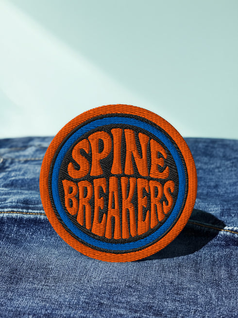 3-inch round embroidered iron-on patch made from a cotton–polyester blend; navy center with blue ring and orange outer ring; stacked orange text reads “SPINE BREAKERS”; merrowed border. Book club patch for paperback addicts, library tote flair, and literary merch collectors; makes a great gift for readers who annotate, dog-ear, and devour novels.