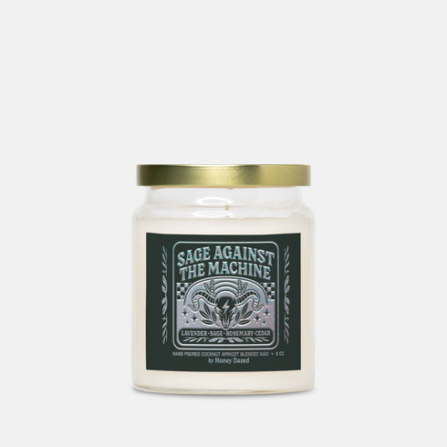 A 9-ounce, hand-poured scented candle in a transparent glass vessel. The candle contains a cotton wick and is filled with a creamy, off-white coconut apricot blended wax. It features a dark, matte finish label with a silver metallic emblem of a ram skull and stylized foliage, with the text "Sage Against The Machine" centered above the scent notes. A shiny gold lid sits atop the glass jar.