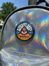 A round pinback button featuring a retro psychedelic design. The central focus is a stylized Eye of Providence in a pink triangle, surrounded by vibrant orange and yellow flames. Behind the triangle are teal and petrol blue sunburst rays. The text "WAKE UP" curves across the top in cream wavy letters, and "THE REVOLUTION" curves along the bottom in orange. The button has a glossy finish and is available in 1.75 inch or 2.25 inch sizes.