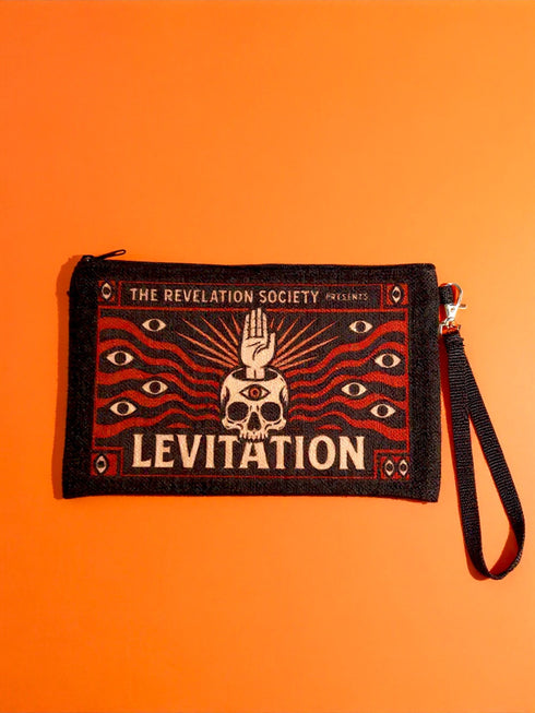 A rectangular makeup bag featuring a vibrant psychedelic print with gothic elements. The fabric texture is clearly visible showing a woven linen-like polyester grain. A black zipper runs across the top edge with a black detachable nylon wrist strap clip on the side, showcasing the approximately nine by six inch dimensions. The print includes high contrast neon colors and trippy swirling patterns typical of maximalist decor.