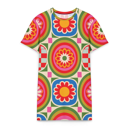 Short sleeve crew neck t-shirt dress on a cream background with an allover retro mod flower medallion print. Bold 60s daisies in red, yellow, and white sit at the center of concentric rainbow rings in lime green, hot pink, orange, and royal blue, with small magenta squares and tiny red checkerboard accents between the motifs. Above-the-knee straight fit silhouette in a 95 percent cotton, 5 percent elastane heavyweight stretch blend. Groovy retro flower power dress for dopamine dressing and easy summer outfi