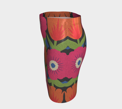 Form-fitting bodycon mini skirt with a mid-rise elastic waistband, falling to mid-thigh in smooth stretch fabric. It features a bold 70s pop art floral print: oversized hot pink flowers with cream scalloped centers, royal blue middles, and fine purple rays, beside a flaming orange tulip, royal blue geometric shapes, and olive green leaves on a black background. The all-over design is a flat dye-sublimated print in vibrant, high-contrast color, available in a smooth knit or glitter knit finish.