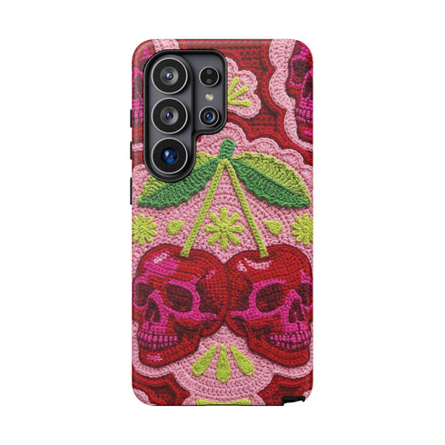 Dual layer matte phone case with a high fidelity 2D print that creates a hyper realistic faux crochet and knit illusion. The central design shows two conjoined cherries styled as bright pink and burgundy human skulls with lime green stems and leaves. The background is a detailed scalloped lace doily pattern in hot pink, deep red, and lime green. Matte finish shell with a black inner TPU lining, precise camera cutout, and open ports. Pastel goth macabre alt fashion phone accessory, made to order.