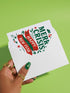 A 5x7 alternative holiday card with a white background and bold, punk-inspired typography. The text reads "Merry Crisis Happy New Fear" in dark green and red. The design features graphic elements like holly, stars, and safety pins, giving it a sarcastic, goth aesthetic. The inside message says "Consider this card your coping mechanism." This snarky, dark humor greeting card is perfect for a funny, unconventional Christmas, capturing a mental health humor and anti-capitalist vibe.