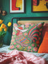 Square throw pillow cover with a printed faux embroidery design of a rooster wearing a white cowboy hat with red stars on a grass green background. The western chicken has a red comb and wattle, yellow beak and feet, and layered feathers in pink, green, orange, blue, and yellow with a rainbow striped tail. Pink and red flowers with yellow centers frame the bird. The stitched look is a flat 2D print on a smooth linen feel polyester cover with a hidden zipper, not raised embroidery.