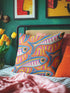 Flat printed square throw pillow cover featuring a faux embroidery texture. The vibrant maximalist design showcases stylized blue, pink, yellow, and white fish swimming in a dynamic, swirling pattern across a bright orange background. The artwork mimics heavy crewelwork yarn and stitching, but the material is a smooth 2D flat print. The pillow is shown as a finished square cover, designed to add bright, colorful eclectic fisherman aesthetic decor to any sofa or seating area.