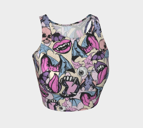 A sleeveless cropped tank top made from stretchy performance knit fabric. The all-over print features a dense, scattered pattern of pastel goth and creepy cute motifs over a light background. Graphics include pink and blue bats in flight, floating eyeballs with blue irises, pink skulls, and glossy vampire lips with sharp white fangs and tongues sticking out. The neckline is a high scoop and the armholes are curved. The fabric comes in either a matte finish or a sparkly silver glitter foil.